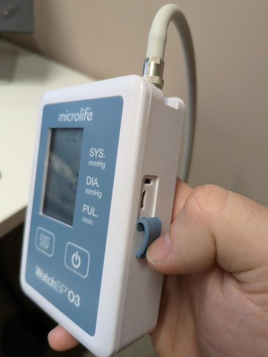 A blood pressure monitor with a flap being held back, revealing a micro-USB port
