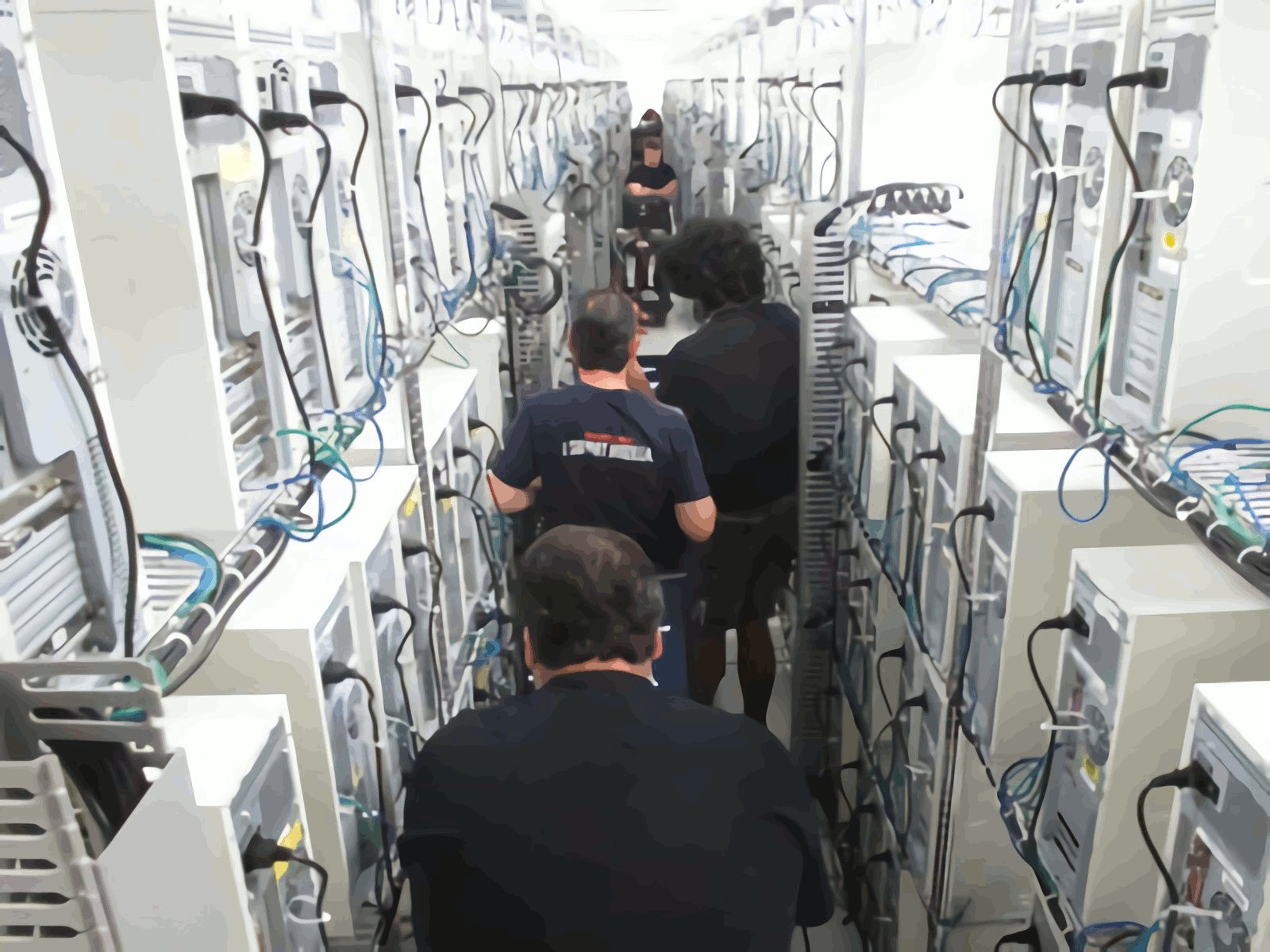 Rows of white desktop computers on kitchen racks, with engineers walking between them